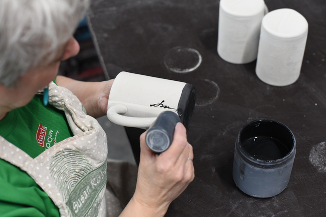 A hand signing a piece of pottery with black paint